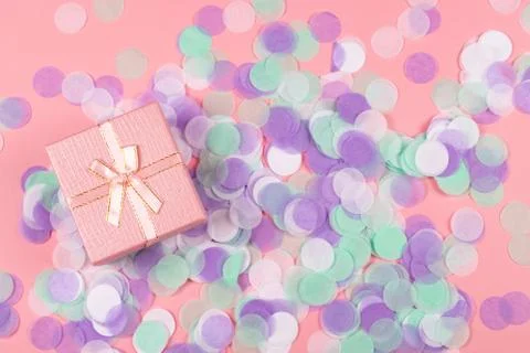 Present box on pink background with multicolored confetti. Stock Photos