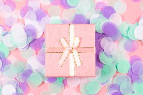 Present box on pink background with multicolored confetti. Stock Photos