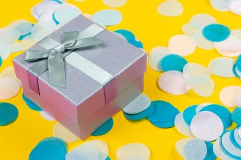 Present box on yellow background with multicolored confetti. Stock Photos