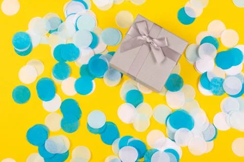 Present box on yellow background with multicolored confetti. Stock Photos