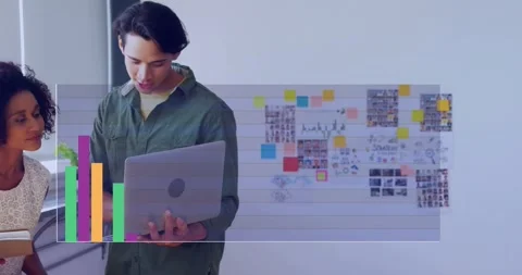Presenting man in green top scrolling laptop at office window, viewing live bar Stock Footage 332285142