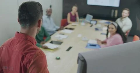Presenting man in red button-down shirt speaking to team in meeting room, Stock Photos
