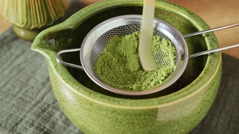 Pressing and sifting bright green matcha powder through metal mesh sieve Stock Footage 345681737