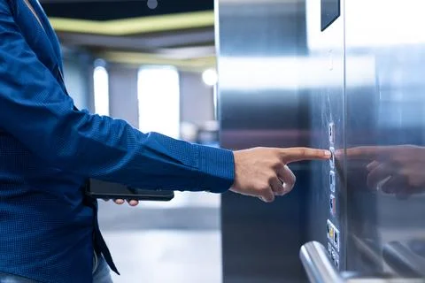 Pressing elevator button, person in blue shirt holding tablet in modern office Foto stock