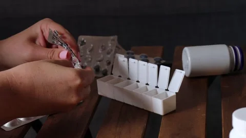 Pressing headache relief tablets from blister into weekly pill organizer on Stock Footage 313794282