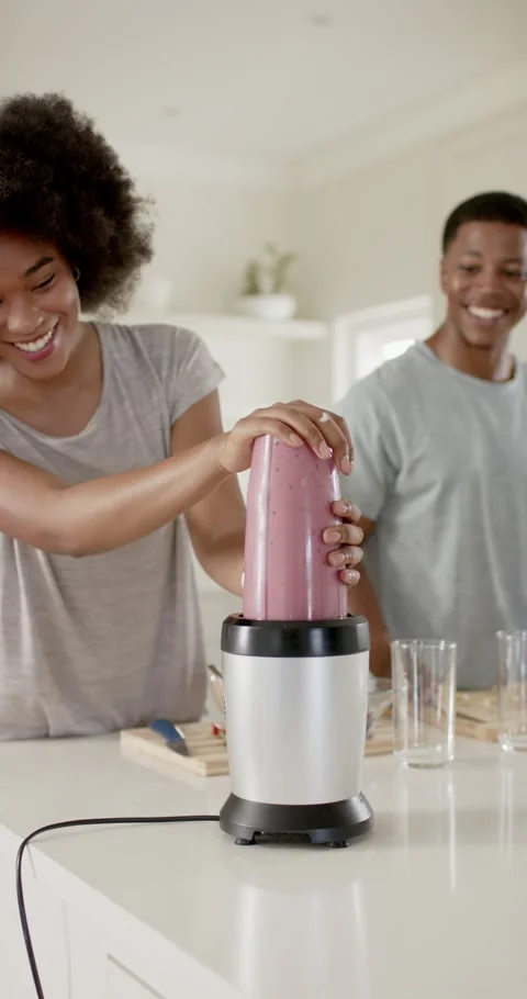 Pressing pink cup onto blender base, woman wearing gray T-shirt blending Video stock 345130603