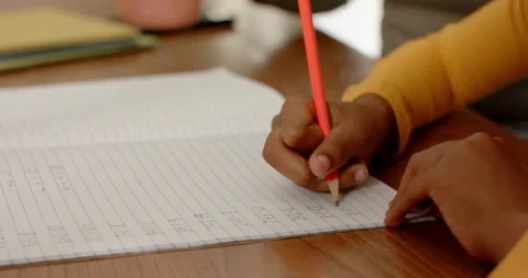 Pressing red pencil, hand is writing in lined notebook for practice on desk with Stock Footage 334923942