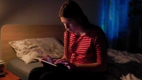 Preteen scrolling tablet screen in bed under neon light reflections Stock-Footage 336669370