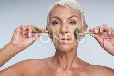 Pretty aged female holding two beauty rollers to her face Stock Photos
