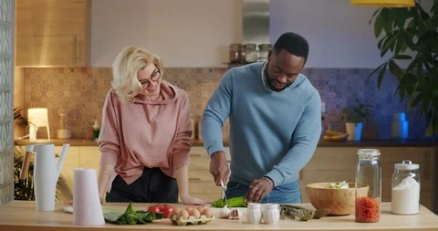 Pretty blonde female looking at her lovely boyfriend cooking healthy salad at Stock Footage 123671002