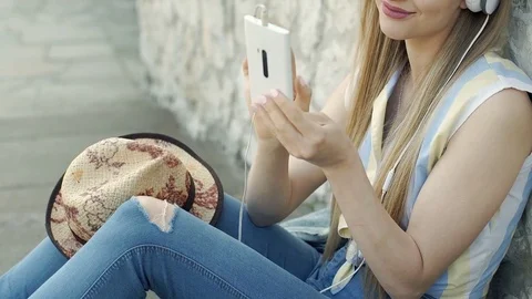 Pretty, blonde girl listening music on headphones and browsing internet on smart Stock Footage