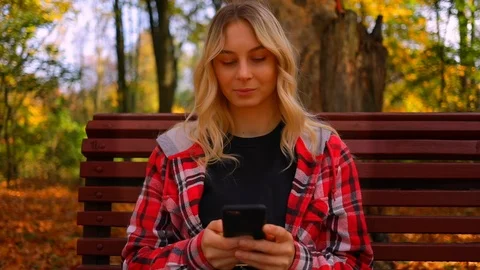 Pretty blonde girl student using a smartphone in a city autumn park, young woman Stock Footage 118990749