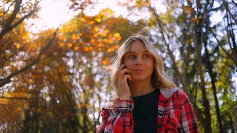 Pretty blonde girl student using a smartphone for conversation in autumn park Stock Footage 119008003