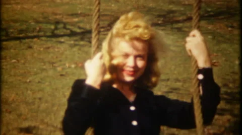 Pretty blonde girl on swing smiles at camera 1950s vintage film home movie 2048 Stock Footage