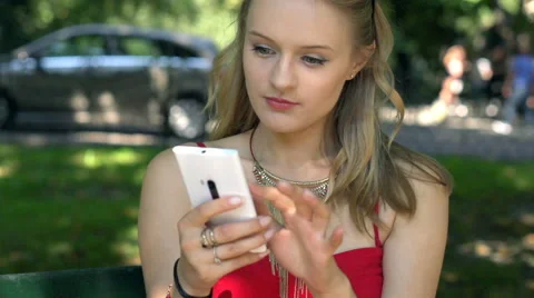 Pretty, blonde girl texting on smartphone in the park, slow motion shot at 240fp Stock Footage