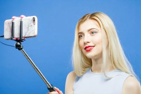 Pretty Blonde is Grimacing While Taking a Photo Using Selfie Stick on Blue Photos