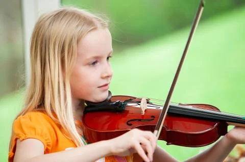 Pretty blonde little girl playing violin with a blurry green background Stock Photos