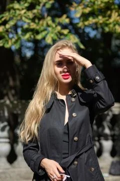 Pretty blonde model with bright makeup wearing black coat and covering her fa Stock Photos