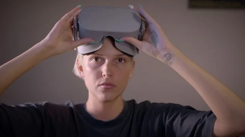Pretty blonde puts on VR glasses and looks around front of camera, oculus go Video stock 114548954