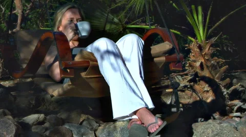 Pretty blonde woman drinks coffee on swing Stock Footage