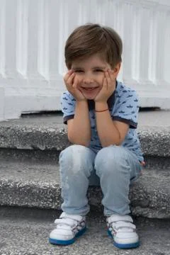 Pretty boy is sitting on the steps and bored. A fashionable kid wearing a blu Stock Photos