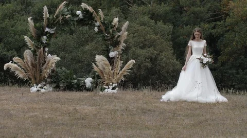 Pretty bride fixes long white wedding dress against arch Stock Footage 123514880