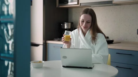 Pretty brunette in a bathrobe, sitting at a table in the kitchen, using a laptop Stock-Footage 252660183