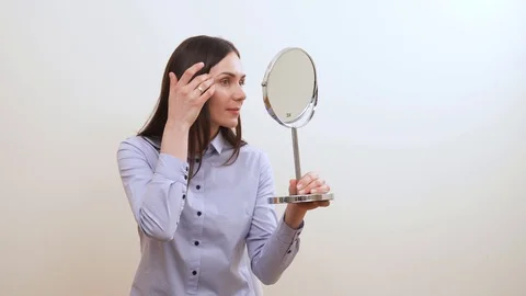 A pretty brunette is looking into the makeup mirror, adjusts her eyebrows Stock Footage 100061930