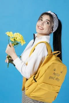 Pretty, brunette student with backpack posing with yellow flower, looking up Stock Photos