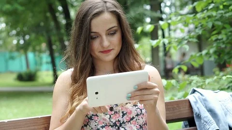 Pretty brunette watching something on tablet and drinking juice in the park, ste Stock-Footage 79348714
