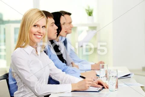 Pretty business lady looking at camera while her colleagues listening to someone Stock Photos