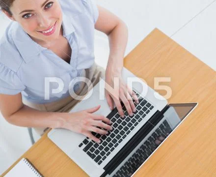 Pretty businesswoman typing on her laptop and smiling up at camera Stock Photos
