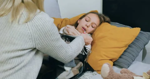 Pretty calm concentrated 40-aged mother checking daughter's temperature on Stock Footage 144621139