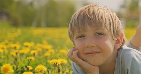Pretty caucasian boy lying on a spring meadow and looks. Happy child lies on  Stock Footage 114385912