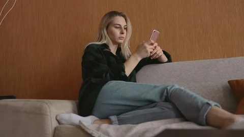 Pretty caucasian model sitting at sofa use smartphone at loft social media 5g Stock Footage 113910423