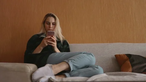 Pretty caucasian model sitting at sofa use smartphone at loft social media 5g Stock Footage 113910943