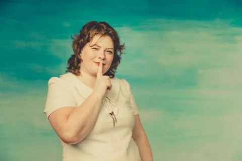 A pretty chubby redhead woman in a white dress raised her index finger to her Stock Photos