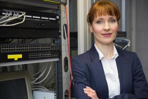 Pretty computer technician smiling at camera beside server Stock Photos
