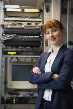 Pretty computer technician smiling at camera beside server Stock Photos