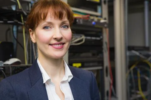 Pretty computer technician smiling at camera beside open server Stock Photos