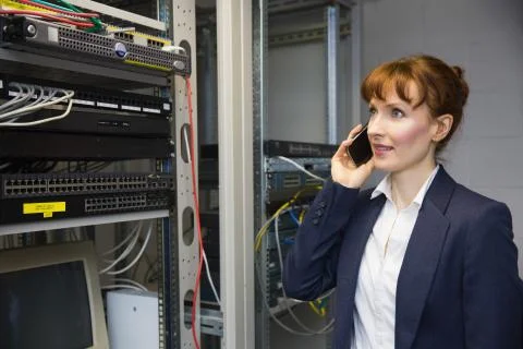 Pretty computer technician talking on phone beside open server Stock Photos