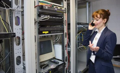 Pretty computer technician talking on phone beside open server Stock Photos
