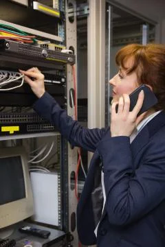 Pretty computer technician talking on phone while fixing server Stock Photos