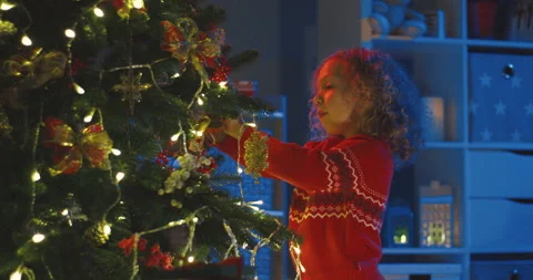 Pretty curly and blond small girl decorating Christmas tree in the dark cozy Stock Footage 139433441
