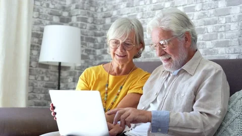 Pretty elderly 70s grey-haired couple resting on couch in living room hold .. Stock Footage 231622742