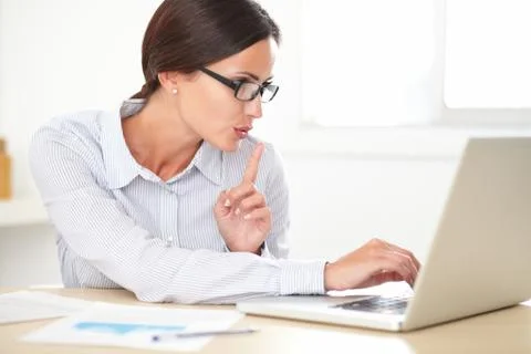 Pretty female executive with spectacles using her laptop while shushing Stock Photos