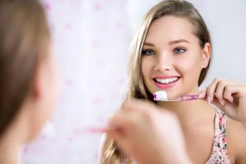 Pretty female looking in mirror while brushing teeth Stock Photos