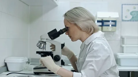 Pretty female with microscope looking at camera in laboratory Vídeos de archivo 77245392