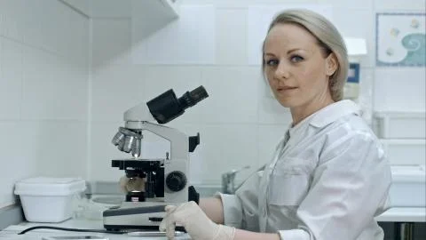 Pretty female with microscope looking at camera in laboratory Stock Photos