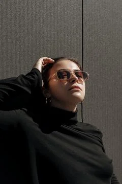 Pretty female model in black pullover posing on the wall background in sun rays Stock Photos